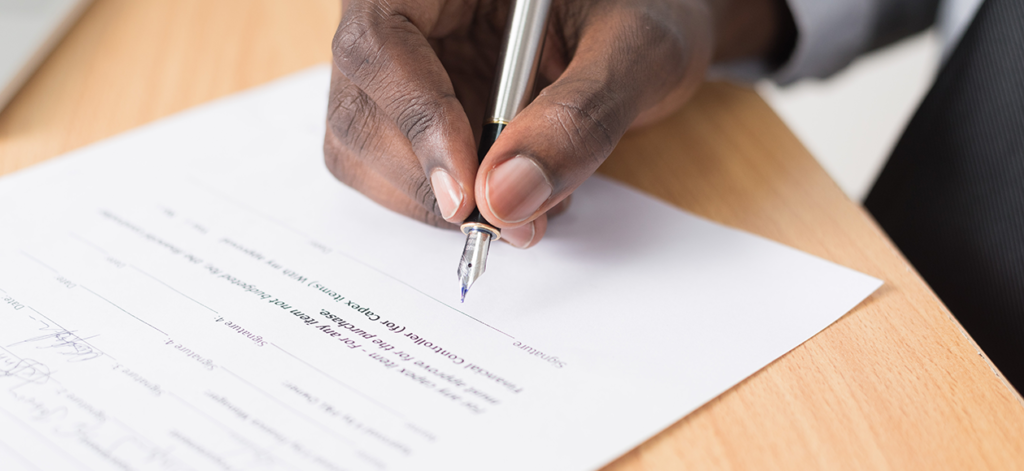 Black male hand holding a pen about to sign freelance contracts