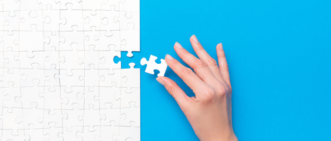 Female hand putting final piece into a white puzzle on a bright blue background